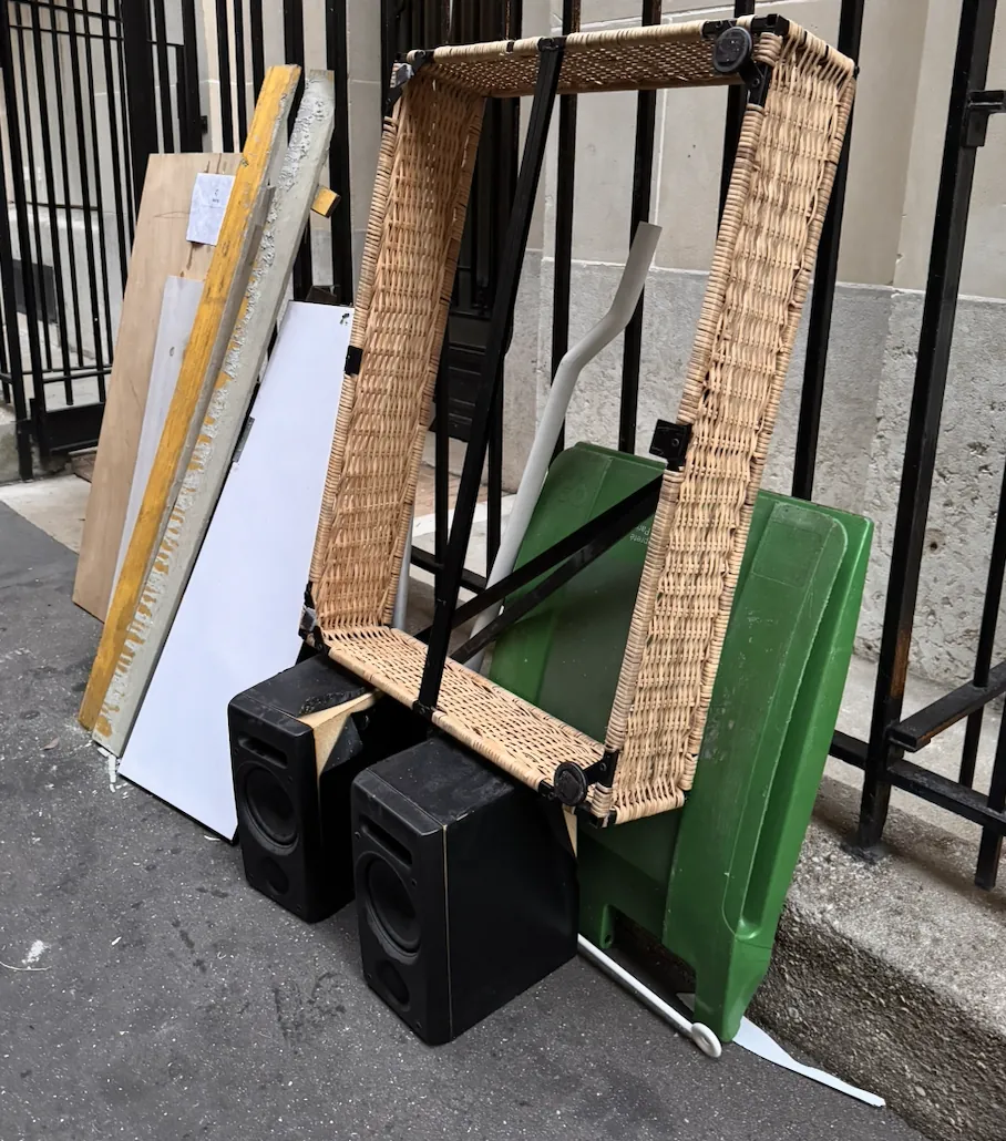 Fauteuil en rotin et enceintes déposés contre une grille parisienne